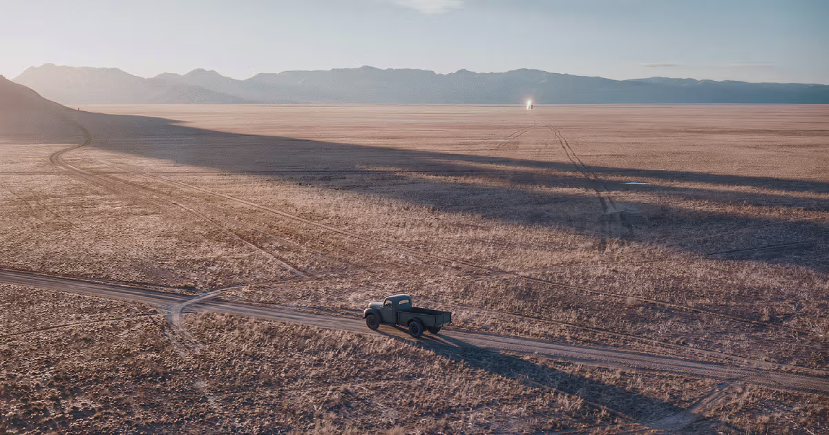 A pickup truck on a track across the wide, dry Plains of San Agustin, with a small glint far out on the plain. Illustration.